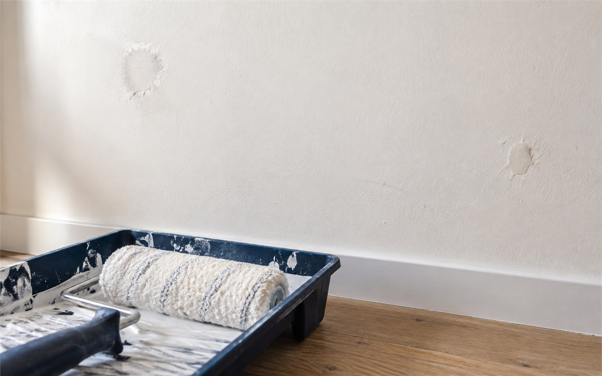 Rouleau et bac de peinture devant un mur blanc cassé avec des reprises d’enduit