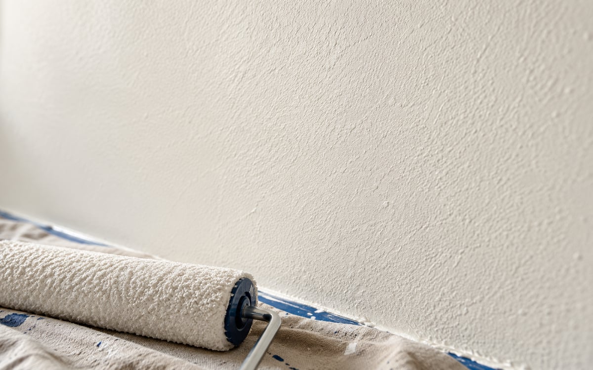 Gros plan d’un mur peint blanc cassé avec un rouleau posé sur une protection